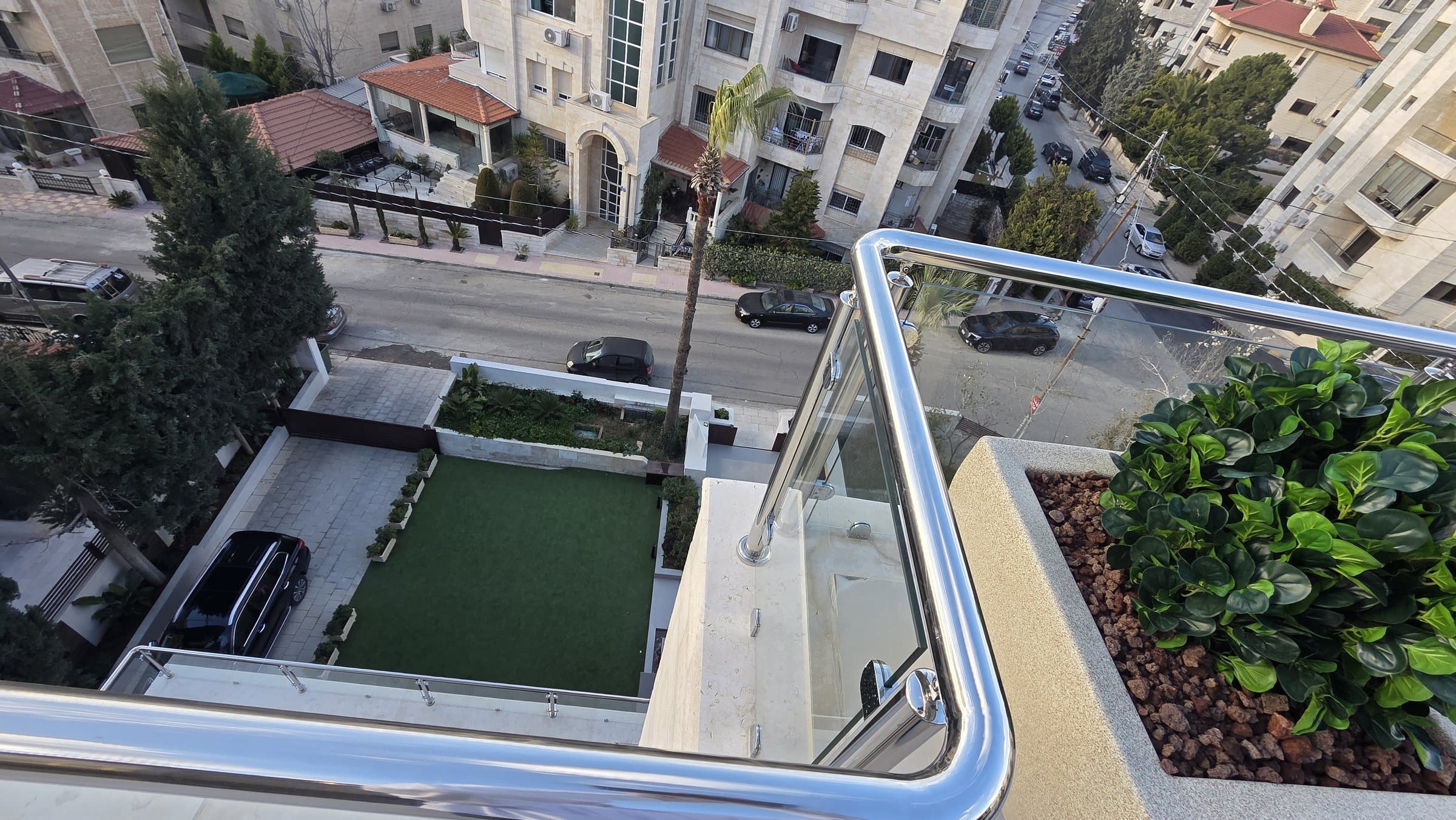 View down from a terrace to the building's private green lawn, landscaped garden, and the wide street below