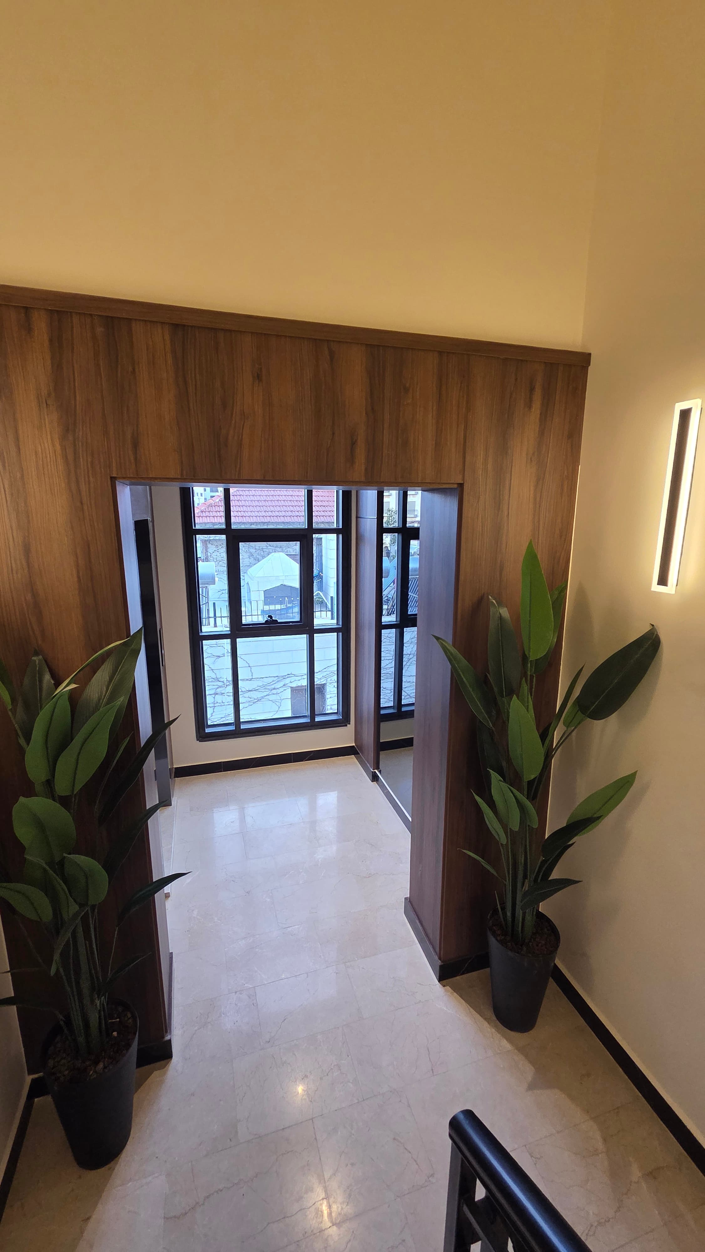 Elevator hall with walnut paneling, integrated sconces, and courtyard window